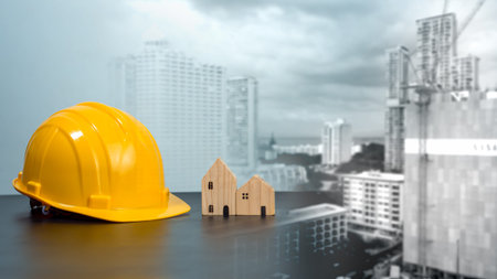Hard hat and wooden house mockup placed at black tabletop on double exposure background of high...