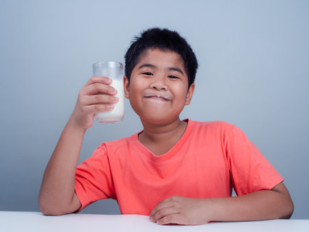 Concept of happy good nutrition, Portrait of a little young handsome kid boy in pink t-shirt, Holding a glass of milk on white background, Smiling of Asian boy with a glass of milk.の写真素材
