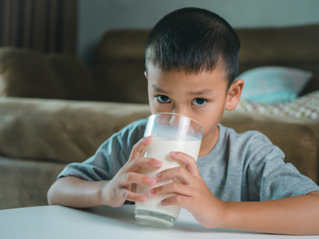 Portrait of a little young handsome kid boy in pink t-shirt, Concept of happy good nutrition, Holding a glass of milk on grey background, Smiling of Asian boy with a glass of milk.の写真素材