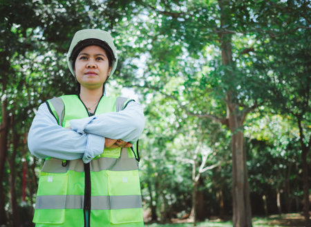 A female engineer wearing a hard hat stands with her arms crossed, Represents readiness to use...