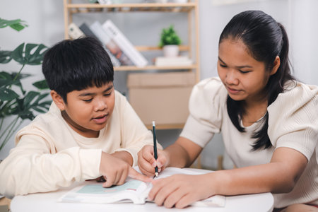 Teacher or sister helping boy writing lesson and learning to write; Female tutor helping little elementary school boy with homework during individual lesson at home; Education home school concept.の写真素材