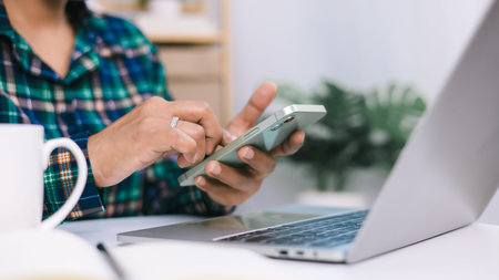 A woman is looking at her cell phone while sitting at a desk. She is focused on her phone, Checking...