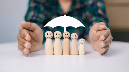 Concept of insurance and protection, insurance planning, Healthcare and finance. Hand and white umbrella give protection to wooden dolls representing family safety protection.の写真素材