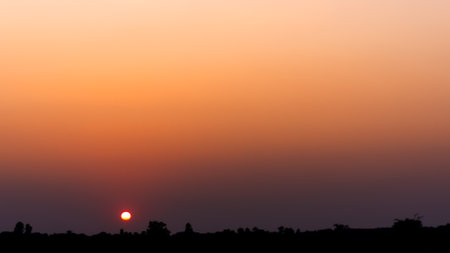 Breathtaking sunset with vivid orange and yellow hues paints the sky, Casting silhouettes over a distant field the scattering clouds add texture and depth, creating a serene twilight ambiance.の写真素材