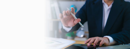 Businessman working at desk using a digital pen and tablet for data analysis, decision-making, business strategy, innovation, financial planning, productivity in a modern office with copy space.の写真素材