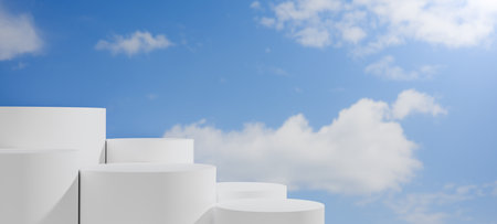 White cylindrical pedestals of different sizes on light gray ground with bright blue sky and clouds, creating serene natural outdoor stage for product display, branding, abstract concepts.の写真素材