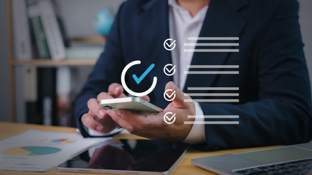 Confident businessman using smartphone to complete online checklist in modern office, symbolizing digital task management, productivity, survey, checkboxes, and business technology.の写真素材