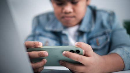 Young person holding green smartphone horizontally, focused on gaming or streaming, with a laptop in foreground, representing digital entertainment and modern youth technology.の写真素材
