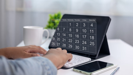 Organized person planning schedule with digital calendar app on tablet, with smartphone, keyboard, and coffee cup on modern workspace, concept of time management and productivity.の写真素材