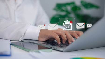 Close up of businessman typing on laptop with multiple email notification icons and alert symbol,...