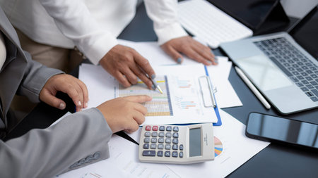 Close-up of two businesswomen analyzing financial charts and data using calculator and laptop in...