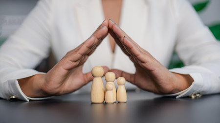 Close-up of businesswoman covering wooden family figures with hands shaped like a roof. Concept of insurance, family protection, safety, care, and financial security for future life.の写真素材