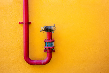 Red fire hydrant pipe on yellow wall background, colorful minimal urban design with bright contrast, architecture detail concept for industrial or creative design.の写真素材