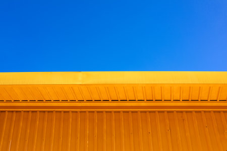 Yellow metal building wall with blue sky in minimal architecture style, clean geometric design background with color contrast for urban and construction concept.の写真素材