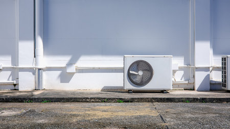 Air conditioner outdoor unit on white wall with sunlight shadow, minimal industrial background, clean architecture detail for energy and technology concept.の写真素材