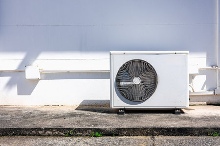 Air conditioner outdoor compressor unit on white wall with sunlight shadow, modern HVAC system concept for energy efficiency and home cooling technology.の写真素材