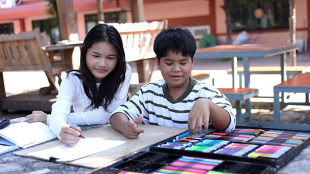 Asian boy and girl drawing together outdoors with colorful art supplies, creativity learning,...