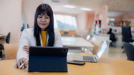 Happy Asian businesswoman working with digital tablet and laptop in modern office. Professional...