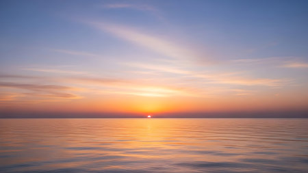 The captures a tranquil ocean horizon at sunset. The sun, a small bright orb, is just above the water, casting a warm orange glow that blends into soft pinks and yellows in the sky. Wispy clouds are scattered across the pastel blue and purple sky. The surface of the sea is calm, reflecting the colors of the sky with gentle, subtle ripples.の素材