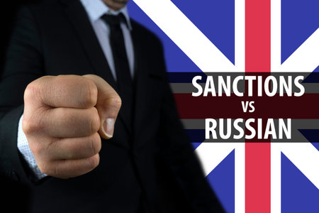 Businessman shows a fist against the background of the English flag and an inscription of sanctions...
