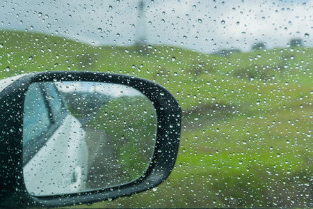 Drops of rain on the window and on the wing mirror; blurred green meadows in the background; shallow depth of fieldの写真素材