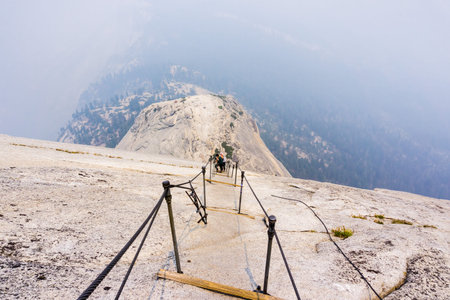 Looking down on the Half Dome cables on a summer day; smoke covering the sub dome and the valley...