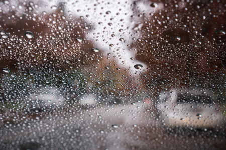 Raindrops on the windshield on a rainy day; street lined up with autumn colored trees in the background; Californiaの写真素材