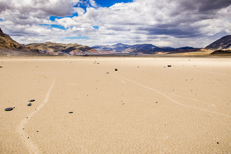 Moving rocks and their tracks at the Racetrack Playa; mountains and clouds scenery in the background; Death Valley National Park, Californiaの写真素材