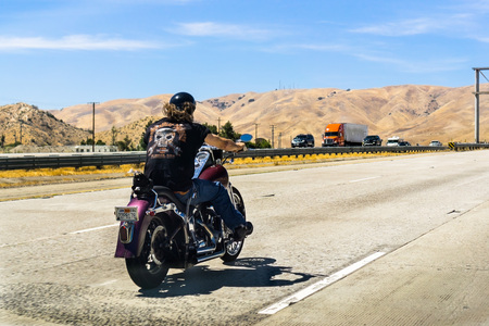 June 10, 2018 Los Angeles / CA / USA - Biker riding a Harley Davidson motorcycle on the interstate; golden hills and blue sky in the backgroundのeditorial素材