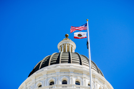 April 14, 2018 Sacramento / CA / USA - The US and the California state flag waving in the wind in front of the dome of the California State Capitolのeditorial素材