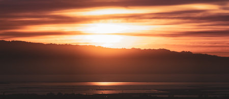 Sun setting behind the Santa Cruz mountains and reflected in the waters of San Francisco Bay;...