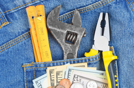 Earnings concept - money and tool in blue jeans pocket