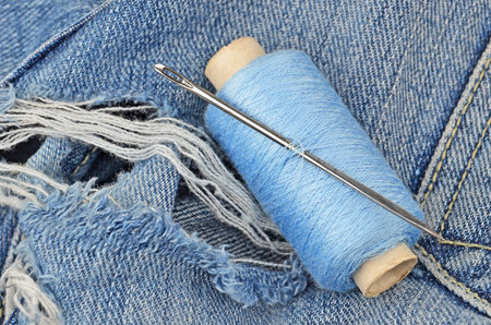 Threads and needle on jeans backround, wear repair concept
