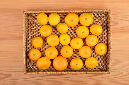 Orange fruit on wickered tray on wooden backgroundの写真素材