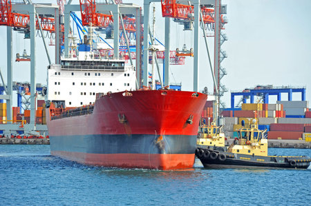 Tugboat assisting bulk cargo ship to harbor quayside
