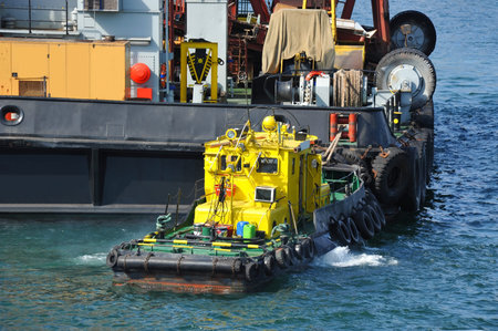 Tugboat assisting floating cargo crane to harbor quayside