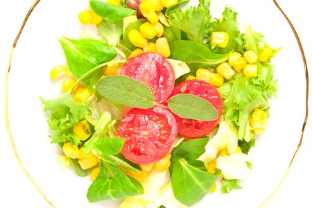 Mixed salad with vegetables, tomatoes and corn on a plate; isolated on whiteの写真素材