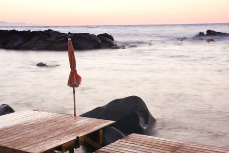 Sea at sunrise with blurred water due to a long exposure and a tied beach umbrella - end of summer conceptの写真素材