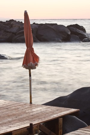 Sea at sunrise with blurred water due to a long exposure and a tied beach umbrella - end of summer conceptの写真素材