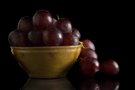 Bunch of black grapes in a ceramic bowl; isolated on black backgroundの写真素材