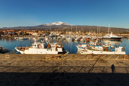 Fishing boats berthed at the Riposto harbour, in Sicily during a sunny day. Etna mount, snow-covered on background.のeditorial素材