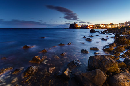Sicily, Italy: the coast of Acicastello (famous sicilian destination) seen at twilight. Castle illuminated on background.の写真素材