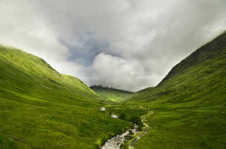 River flowing through a valley in the scottish highlands, the mountains are covered in cloudsの写真素材
