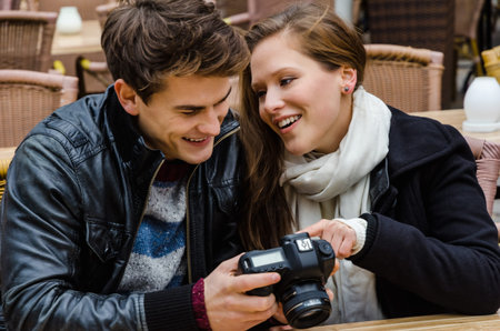 Happy young woman looking at photographs on digital camera with man at outdoor restaurant