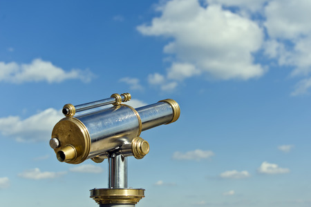coin operated antique telesecope with brass and metal elements in front of a blue cloudy skyの写真素材