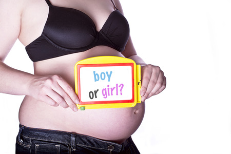 pregnant woman clothed in black bra and jeans holding a toy slate with text "boy or girl" in front of her bellyの写真素材
