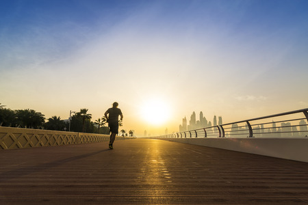 jogger on an empty boardwalk running against the sun with the skyline of Dubai in the background, UAE, Middle Eastの写真素材