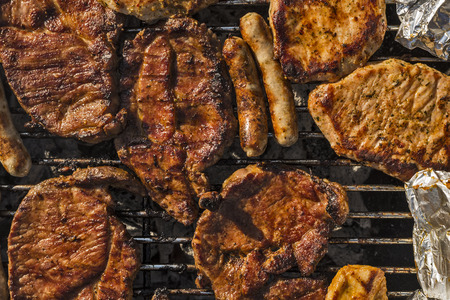 different kinds of meat and sausages on a barbecue grill seen from top viewの写真素材
