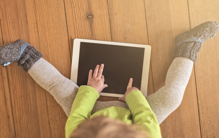 top view of a toddler in green shirt playing with a tablet device on a wooden floorの写真素材