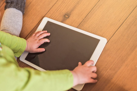 toddler playing with tablet device on a wooden floor